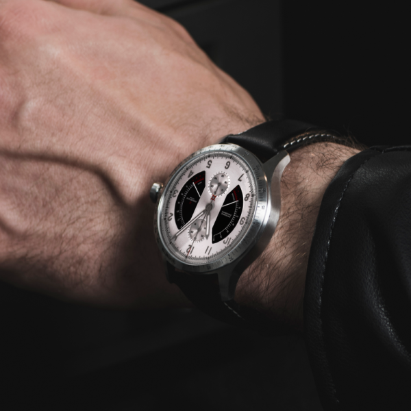 Wristwatch with silver case, black leather strap, white dial, sub-dials, worn with black jacket.