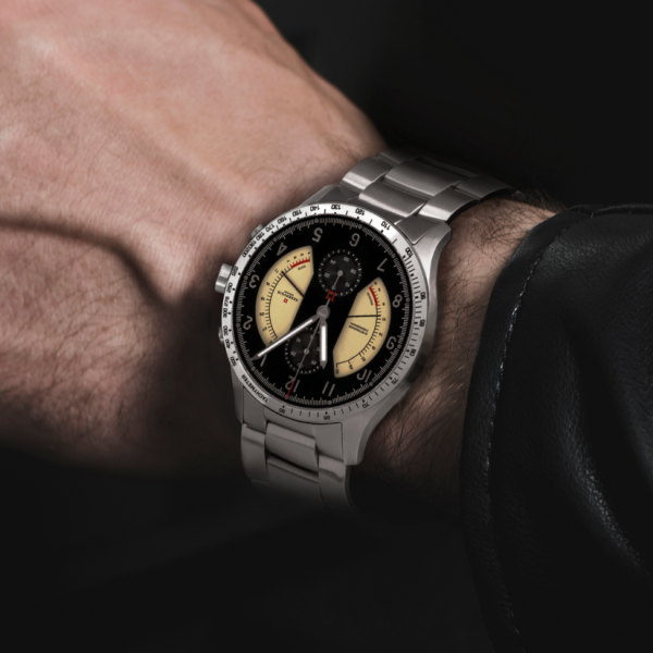 Wrist wearing a stainless steel watch with black dial, beige sub-dials, tachymeter bezel.
