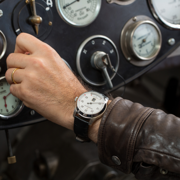 Person wearing a wristwatch adjusting control in vintage vehicle cockpit, dials and gauges visible.