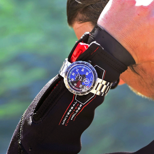 Wrist in a diving suit with a Universal Computer Holder and a diver's watch with a blue dial.