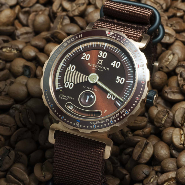 Wristwatch with brown face, white markings, on coffee beans, metallic casing, and brown fabric strap.