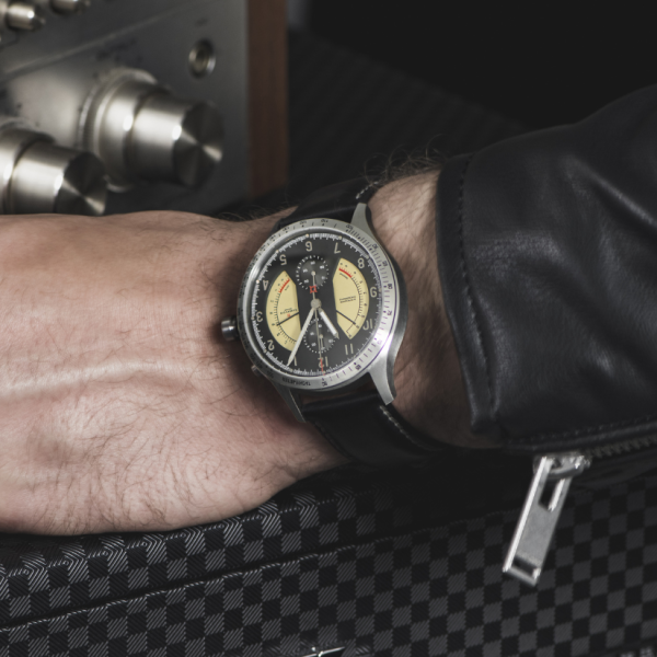 Wristwatch with yellow and black dial, stainless steel bezel, black leather strap, person in leather jacket.