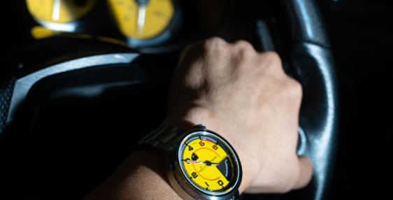 Une personne tient une roue et porte une montre à cadran jaune ; tableau de bord d'une voiture avec des cadrans jaunes visibles.
